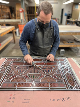 Michael McEllhattan, Renaissance Glassworks manager, resoldering a restored panel for the St. Rose of Lima window.